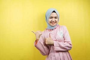 Cheerful beautiful young muslim woman, with hand pointing at empty space, promoting something, isolated photo