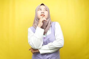 Hermosa joven musulmana asiática pensando, buscando ideas, buscando soluciones a los problemas, con las manos sosteniendo las mejillas, aisladas sobre fondo amarillo