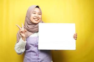 Bastante joven mujer musulmana alegre sosteniendo pancarta vacía en blanco, cartel, tablero blanco, tablero de letrero en blanco, tablero de anuncio blanco, presentando algo en el espacio de la copia, promoción foto