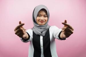 Beautiful young asian muslim woman smiling, with korean love sign hand, hand close to camera, isolated on pink background photo