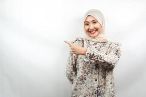 Hermosa joven musulmana asiática con las manos apuntando hacia el espacio vacío presentando algo, sonriendo confiado, entusiasta, alegre, mirando a la cámara, aislado sobre fondo blanco, concepto de publicidad foto