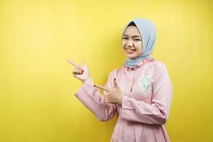 Cheerful beautiful young muslim woman, with hand pointing at empty space, promoting something, isolated