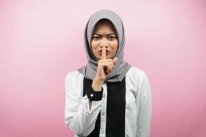 Hermosa joven musulmana asiática con el dedo en la boca, diciendo que se calle, no hagas ruido, baja la voz, no hables, aislado sobre fondo rosa foto
