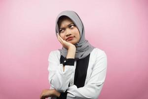 Beautiful asian young muslim woman thinking, looking for ideas, looking for solutions to problems, with hands holding cheeks, isolated on pink background photo