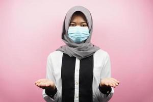 Muslim woman wearing medical mask, hands presenting something, isolated on pink background photo