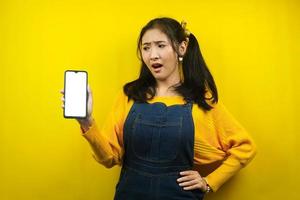 Pretty and cute young woman surprised, shocked, wow expression, hands holding smartphone, with blank or white screen smartphone, promoting app, promoting product, advertisement, isolated photo