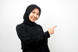 Beautiful young asian muslim woman with hands pointing empty space presenting something, smiling confident, enthusiastic, cheerful, looking at camera, isolated on white background, advertising concept photo