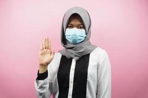 Mujer musulmana con máscara médica con signo de mano abierta, ¿cómo estás? Hola, signo de mano, aislado sobre fondo rosa. foto