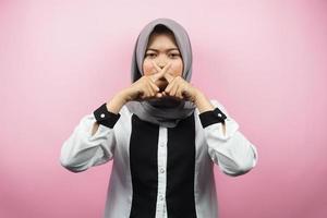 Beautiful asian young muslim woman with finger on mouth, telling to be quiet, don't make noise, lower your voice, don't talk, isolated on pink background