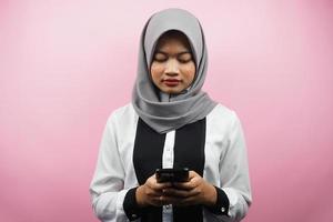 Beautiful asian young Muslim woman holding smartphone isolated on pink background photo