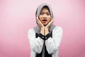 Hermosa joven mujer musulmana asiática conmocionada, sorprendida, wow expresión, con la mano que sostiene la mejilla frente a la cámara aislada sobre fondo rosa foto