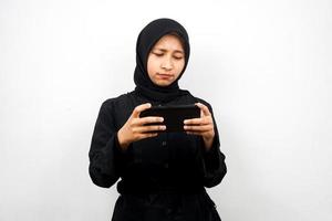 Beautiful asian young muslim woman with hand holding smartphone, playing game, sad, defeat, unhappy, isolated on white background, advertising concept photo