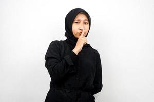 Beautiful asian young muslim woman with finger on mouth, telling to be quiet, don't make noise, lower your voice, don't talk, isolated on white background photo