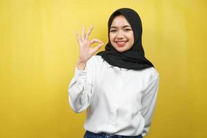 Hermosa joven mujer musulmana asiática sonriendo confiada, entusiasta y alegre con las manos signo de ok, éxito, buen trabajo, signo de éxito, aislado sobre fondo amarillo foto