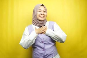 Hermosa joven mujer musulmana asiática sonriendo sorprendida y alegre, con las manos sosteniendo el pecho, emocionada, sin esperar, mirando a la cámara aislada sobre fondo amarillo foto