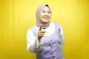 Hermosa joven musulmana asiática sonriendo confiada y alegre, con las manos apuntando a la cámara, apuntando a la audiencia, apuntando al cliente, aislado sobre fondo amarillo foto