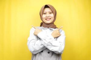 Beautiful young asian muslim woman smiling confident, enthusiastic, cheerful with hands pointing  empty space presenting something, looking at camera isolated on yellow background, advertising concept photo