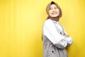 Beautiful young asian muslim woman confident and cheerful looking empty space presenting something, isolated on yellow background photo