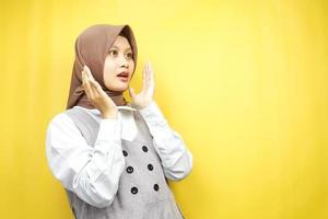 Beautiful young asian muslim woman shocked, disbelieving, surprised, looking at an empty space presenting something isolated on a yellow background photo