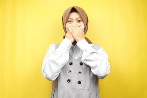 Beautiful young asian muslim woman shocked, surprised, disbelieving, getting shocking information, with hands covering mouth isolated on yellow background photo