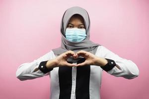 Muslim woman using medical masks with love hands, anti corona virus movement, anti covid-19 movement, health movement using masks, isolated on pink background photo