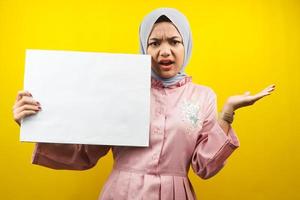 Bastante joven musulmana sorprendida, mano sosteniendo pancarta vacía en blanco, cartel, tablero blanco, tablero de letrero en blanco, tablero de anuncio blanco, presentando algo en el espacio de la copia, promoción foto