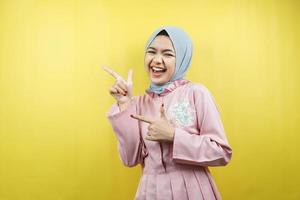 Cheerful beautiful young muslim woman, pointing to empty space, promoting something, isolated photo