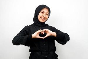 Hermosa joven musulmana asiática sonriendo confiada, entusiasta y alegre con las manos en señal de amor, afecto, feliz, en el pecho aislado sobre fondo blanco. foto