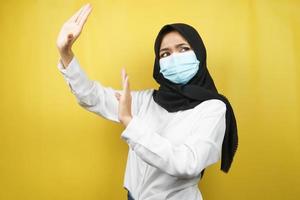 Mujer musulmana con máscara médica con la mano rechazando algo, la mano deteniendo algo, la mano que no le gusta algo, aislado sobre fondo amarillo