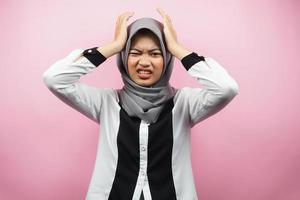 Beautiful young asian muslim woman stressed, shocked, dizzy, unhappy, many problems, want solution, with hands holding head isolated on pink background