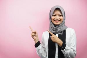 Beautiful young asian muslim woman smiling confident, enthusiastic and cheerful with hands pointing  empty space presenting something facing camera isolated on pink background, advertising concept photo