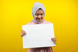 Bastante joven mujer musulmana alegre sosteniendo pancarta vacía en blanco, cartel, tablero blanco, tablero de letrero en blanco, tablero de anuncio blanco, presentando algo en el espacio de la copia, promoción foto