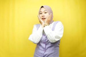 Beautiful young asian muslim woman shocked, surprised, wow expression, with hand holding cheek facing camera isolated on yellow background photo