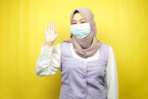 Muslim woman wearing medical mask with open hand sign, how are you doing, hello sign hand, isolated on yellow background photo