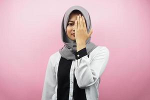 Hermosa joven musulmana asiática con la mano cubriendo un ojo mirando a la cámara aislada sobre fondo de color rosa foto