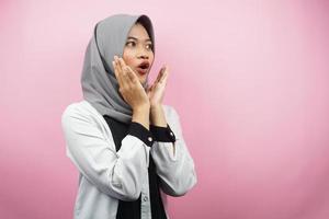 Beautiful young asian muslim woman shocked, disbelieving, surprised, looking at an empty space presenting something isolated on a pink background