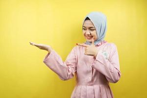 Cheerful beautiful young muslim woman, with hand pointing at empty space, promoting something, isolated photo