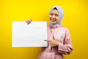 Bastante joven mujer musulmana alegre sosteniendo pancarta vacía en blanco, cartel, tablero blanco, tablero de letrero en blanco, tablero de anuncio blanco, presentando algo en el espacio de la copia, promoción foto