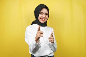 Beautiful young asian muslim woman smiling confident, enthusiastic and cheerful with hands pointing at camera, hands pointing at audience, facing camera isolated on yellow background