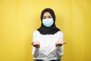 Mujer musulmana con máscara médica, manos presentando algo, aislado sobre fondo amarillo foto