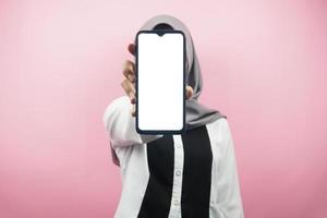 Muslim woman with hands holding smartphone, presenting app, presenting something, isolated on pink background, advertising concept photo