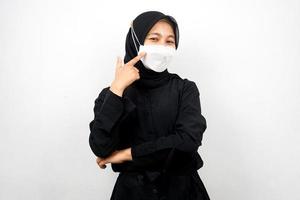 Mujer musulmana con máscara blanca, con la mano apuntando a la máscara, prevenir el gesto del virus corona, prevenir el covid-19, aislado sobre fondo blanco.