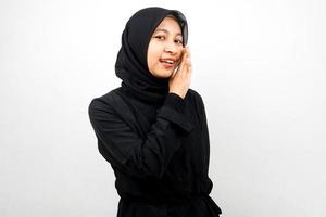 Beautiful young asian muslim woman smiling confidently and excitedly close to camera, whispering, telling secrets, speaking quietly, silent, isolated on white background photo