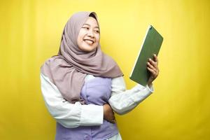 Beautiful young asian muslim woman smiling, excited and cheerful holding tablet, isolated on yellow background photo