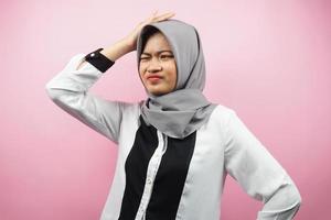 Beautiful young asian muslim woman stressed, dizzy, have a problem, feeling depressed, with hands holding head isolated on pink background photo