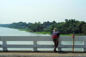 Rear view of man looks for the fish in  the river for fishing by the wooden gun with landscape in bakground photo