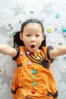 Retrato de niña asiática arrojar y comer dulces y chocolate de trick or treat con tema de halloween en segundo plano. foto
