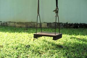 Closeup old wooden swing hanging from the tree in the backyard garden photo