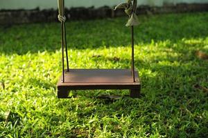 Closeup old wooden swing hanging from the tree in the backyard garden photo