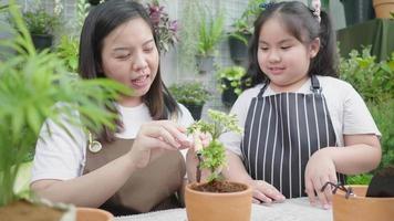 Front view of Happy Asian mom teaching her kid to plant a small tree in flowerpot, using a shovel to plant a tree in a flowerpot. Family activity on the weekend. Gardening tools video